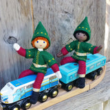Red haired Kindness elf and black kindness elf dolls sitting on a toy train.